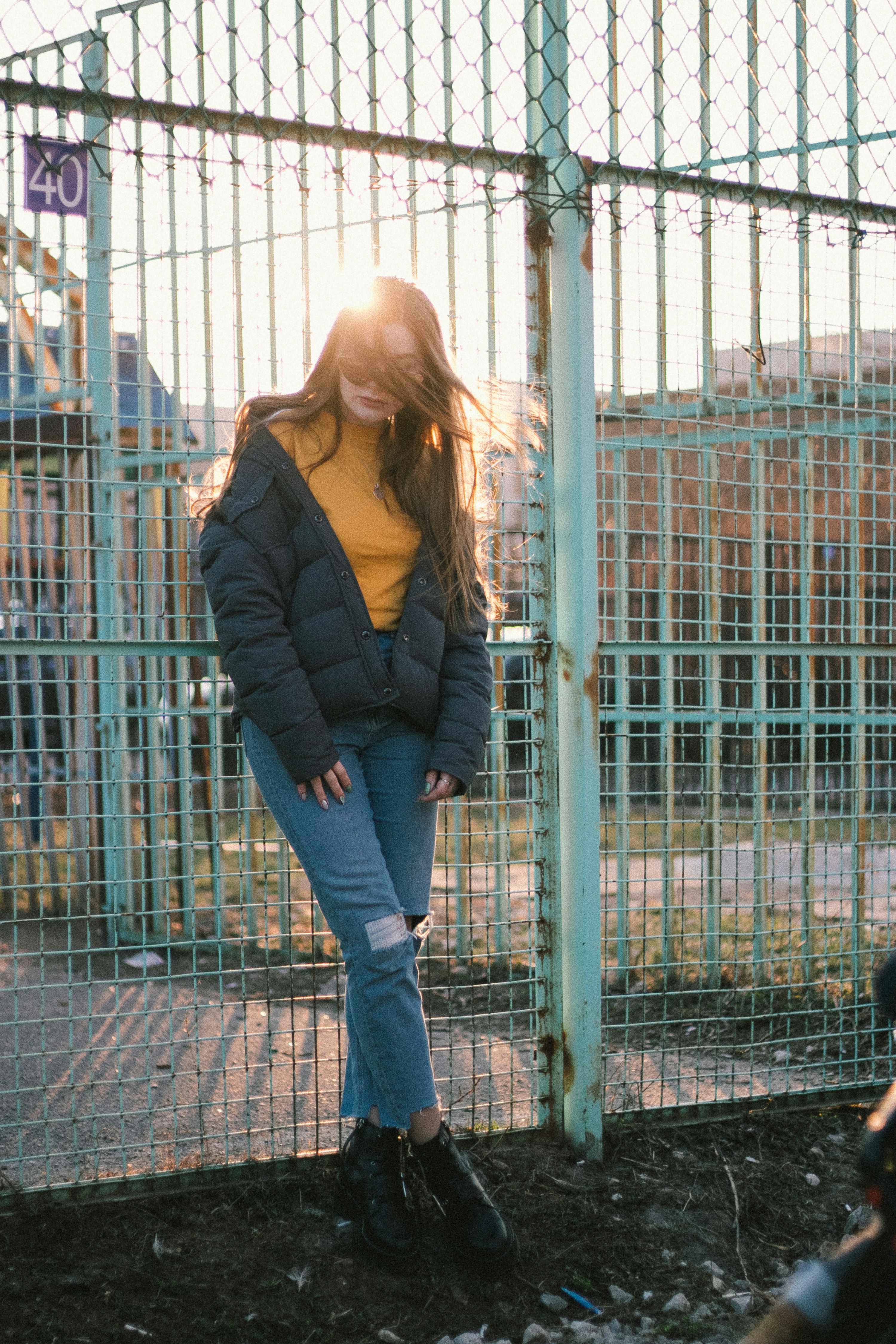 woman in black jacket and blue denim jeans standing near blue metal fence during daytime